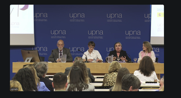 Cuatro personas sentadas en una mesa de debate frente a un público, con un telón de fondo azul que muestra el logotipo y el texto "upna". Uno de los panelistas habla mientras los demás escuchan durante un acto sobre novedades jurídicas recientes. Congreso Internacional sobre la Ley 8/2021