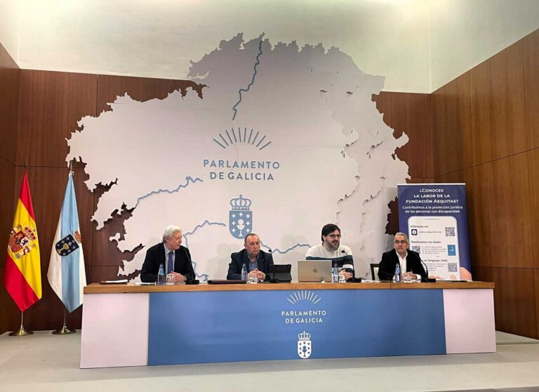 Cuatro hombres están sentados en una mesa de reuniones frente a un gran mapa en el que se lee «Parlamento de Galicia». A la izquierda se ven las banderas de España y de Galicia, y a la derecha hay un cartel informativo. Los derechos fundamentales de las personas con discapacidad